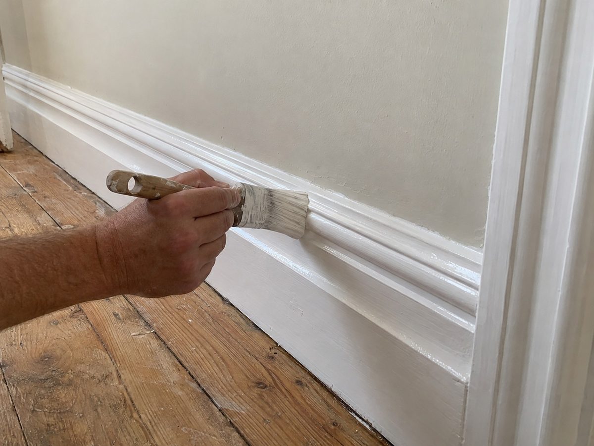 A brush glossing a skirting board above bare floorboards