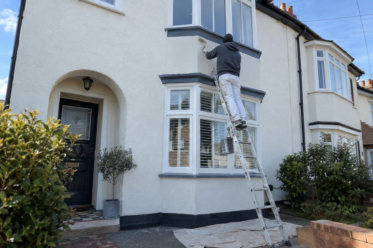 A detached house with an arched porch, a decorator on a ladder at the upper render
