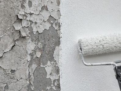 A roller taking fresh masonry coating over a wall of badly flaking old paint, the two halves side by side